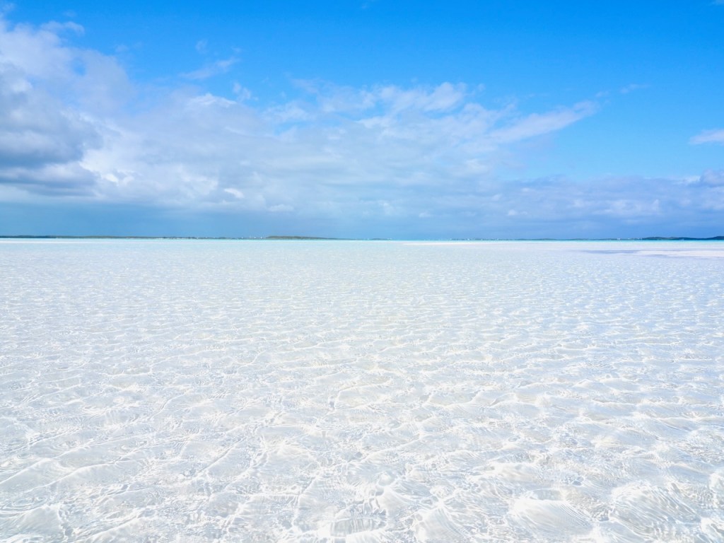 Exuma Bahams beach where clear blue Caribbean water extending to the horizon where it meets brilliant blue sky